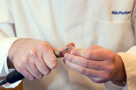Handwerkliche Bearbeitung eines Hörgeräts durch einen Hörakustiker mit Spezialwerkzeug.